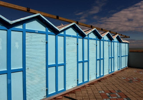 Immagine con cabine, azzurro, nuvole, mare, cielo, spiaggia, legno, piastrelle, porte, acqua, blu, triangoli, fila, prospettiva, mattonelle, geometrie